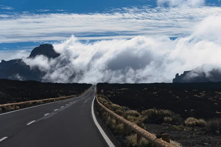 A road leads through a volcanic landscape towards mountains